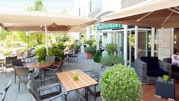 An outdoor seating area with tables and chairs, a sign for a restaurant, and potted plants.