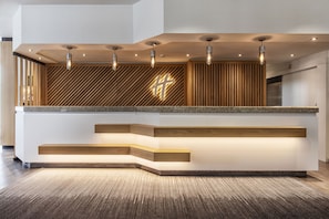 A reception desk with a modern design, featuring a wooden slat wall and a prominent illuminated cross. - Holiday Inn Düsseldorf - Neuss by IHG (Neuss)