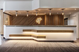 Un comptoir d’accueil au design moderne, agrémenté d’un mur à lattes en bois et d’une grande croix lumineuse.