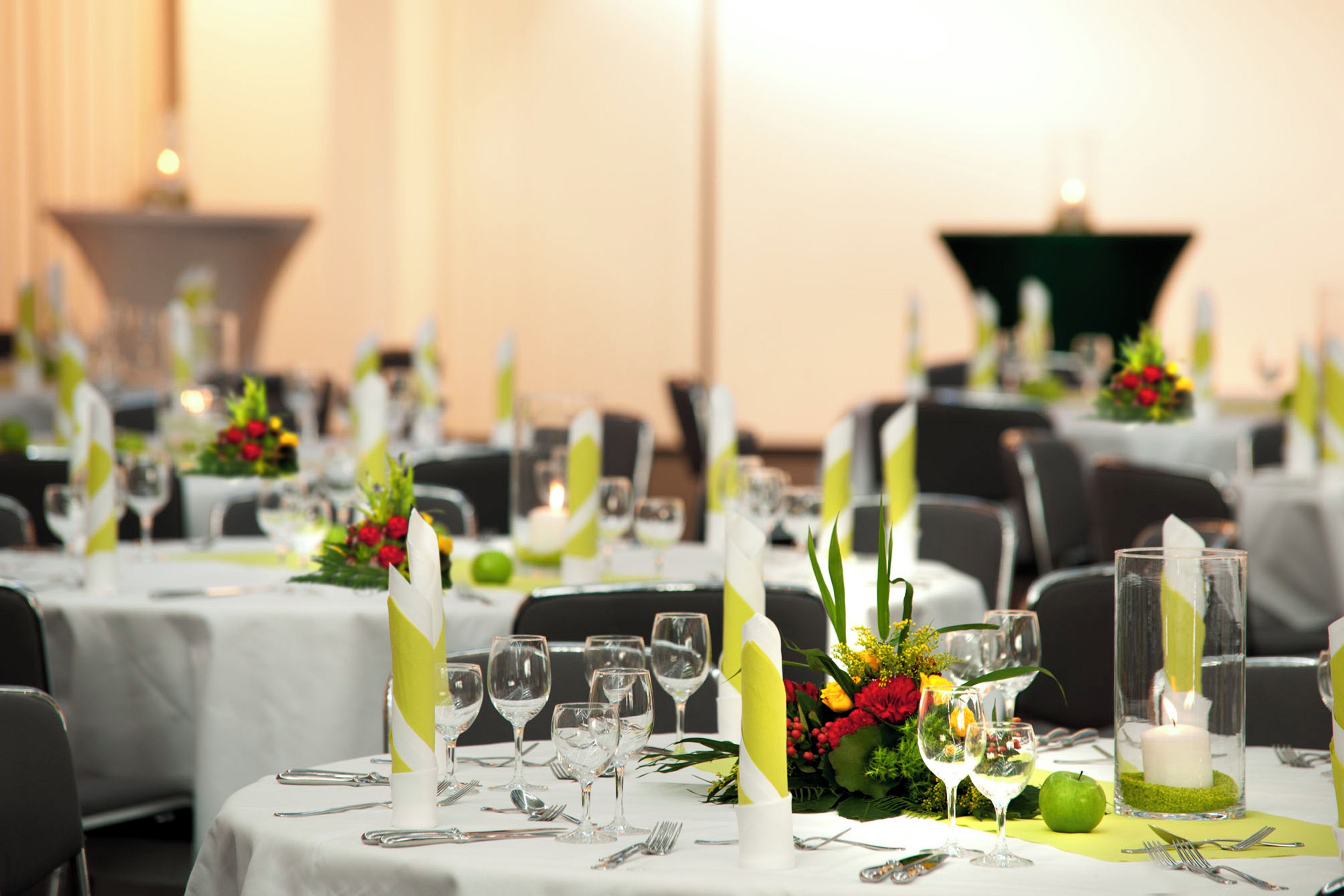 Un salón de banquetes con mesas redondas dispuestas para comer, cada una con un centro de mesa, vasos y cubiertos.