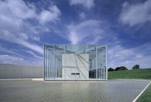 A modern glass building with a geometric design, situated on a flat surface with a clear sky in the background.