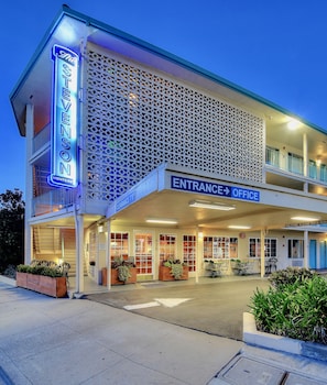 A motel with a neon sign, an entrance office, and a covered outdoor area with plants.