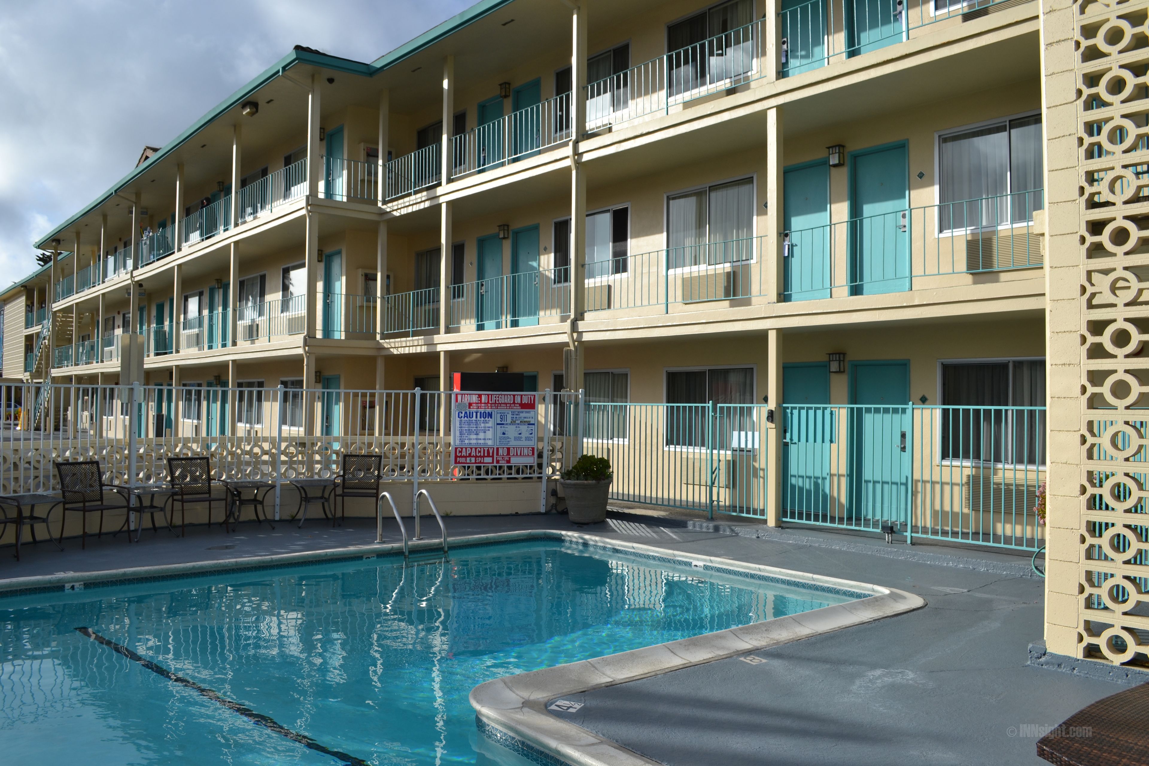 A multi-story hotel with a swimming pool, outdoor seating, and balconies.