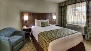 A hotel room with a large bed, a chair, a nightstand, and a window with curtains. - The Stevenson Monterey (Monterey)