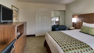 A hotel room with a bed, a TV on a wooden dresser, a desk with a chair, and a bathroom visible through an open door.