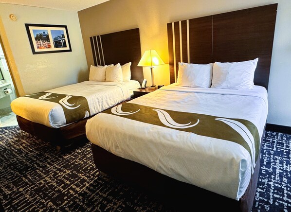 A hotel room with two beds, a nightstand with a lamp, a framed picture on the wall, and a patterned carpet.