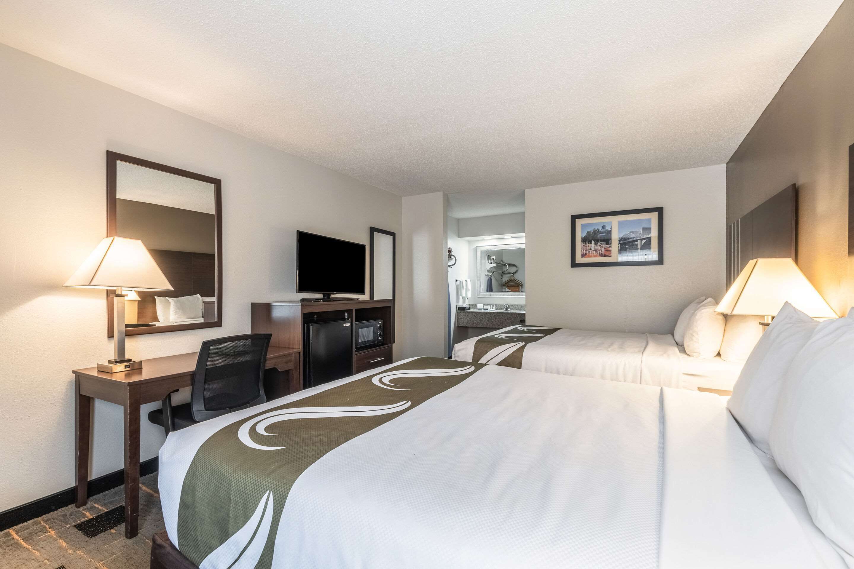A hotel room with two beds, a desk, a television, and a bathroom visible through an open door.