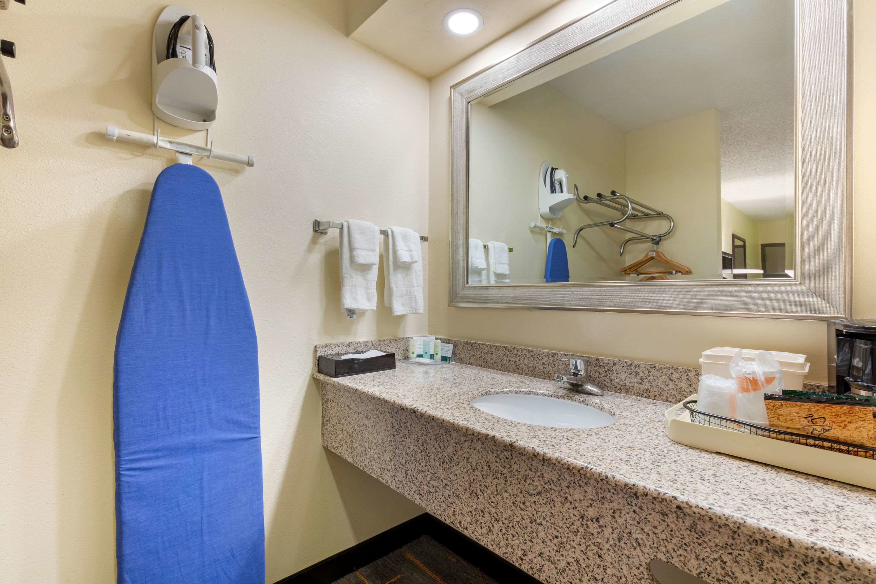 A hotel bathroom with a sink, mirror, towel rack, and ironing board.