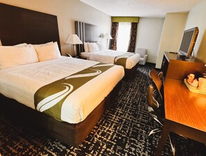 A hotel room with two beds, a desk, a chair, a television, and a window with curtains.