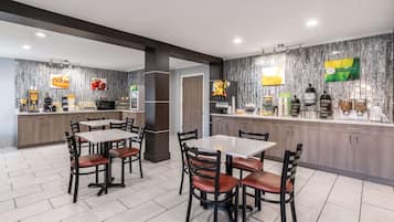 A modern hotel lobby with a dining area, a reception desk, and a kitchen counter with various amenities.