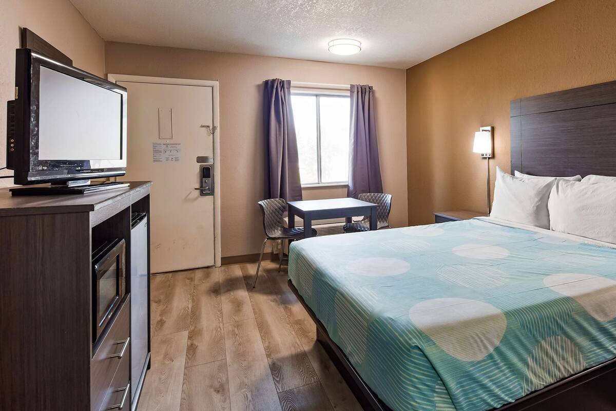 A hotel room with a bed, a desk, a television, and a window with curtains.
