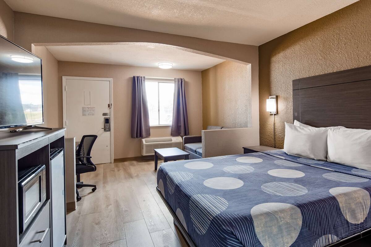 A hotel room with a bed, desk, chair, and a television.