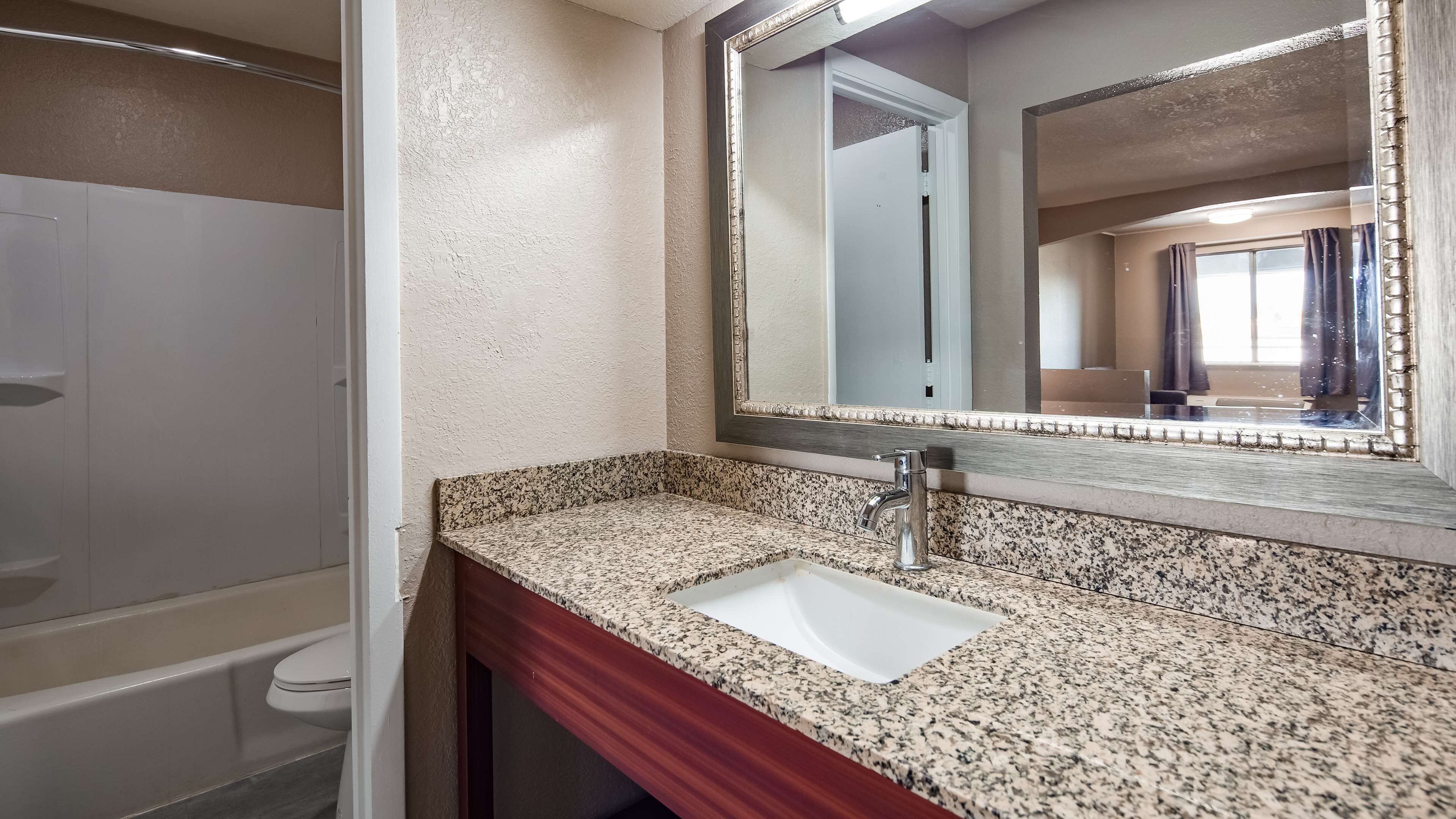 A bathroom with a granite countertop sink, a mirror, and a toilet.