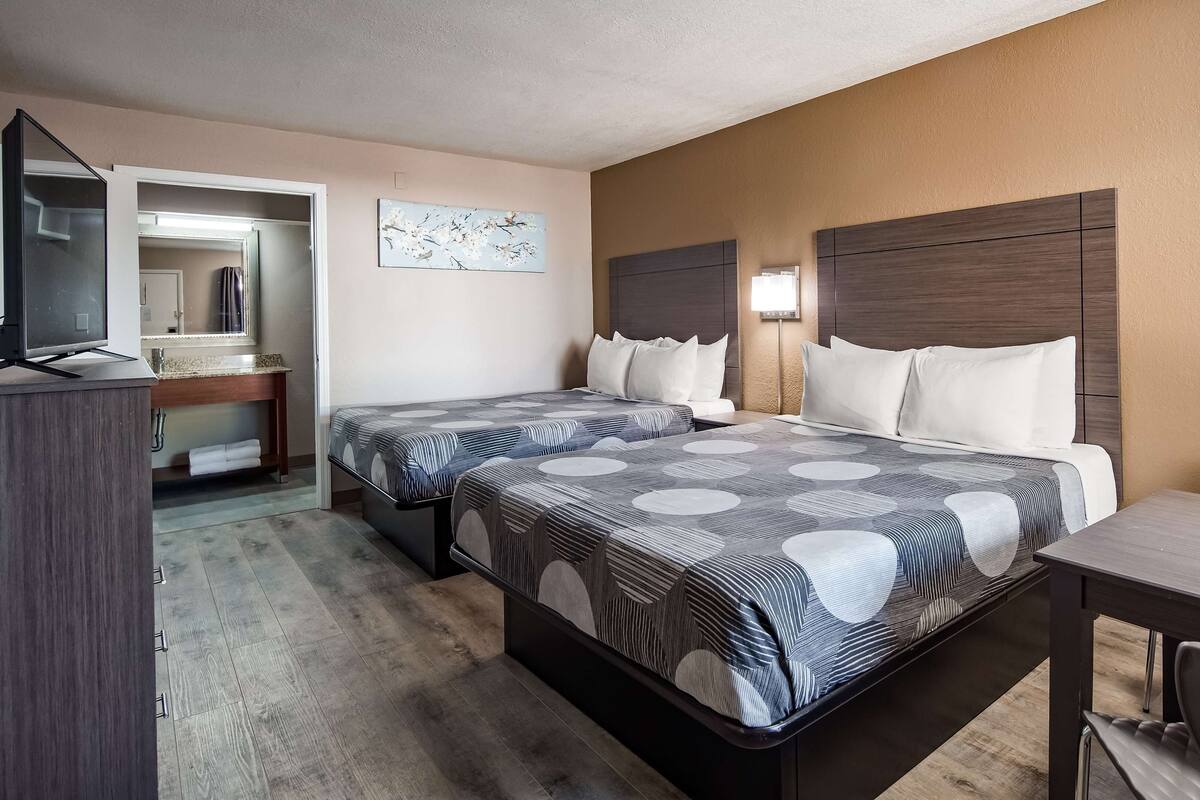 A hotel room with two beds, a desk, a chair, and a TV.
