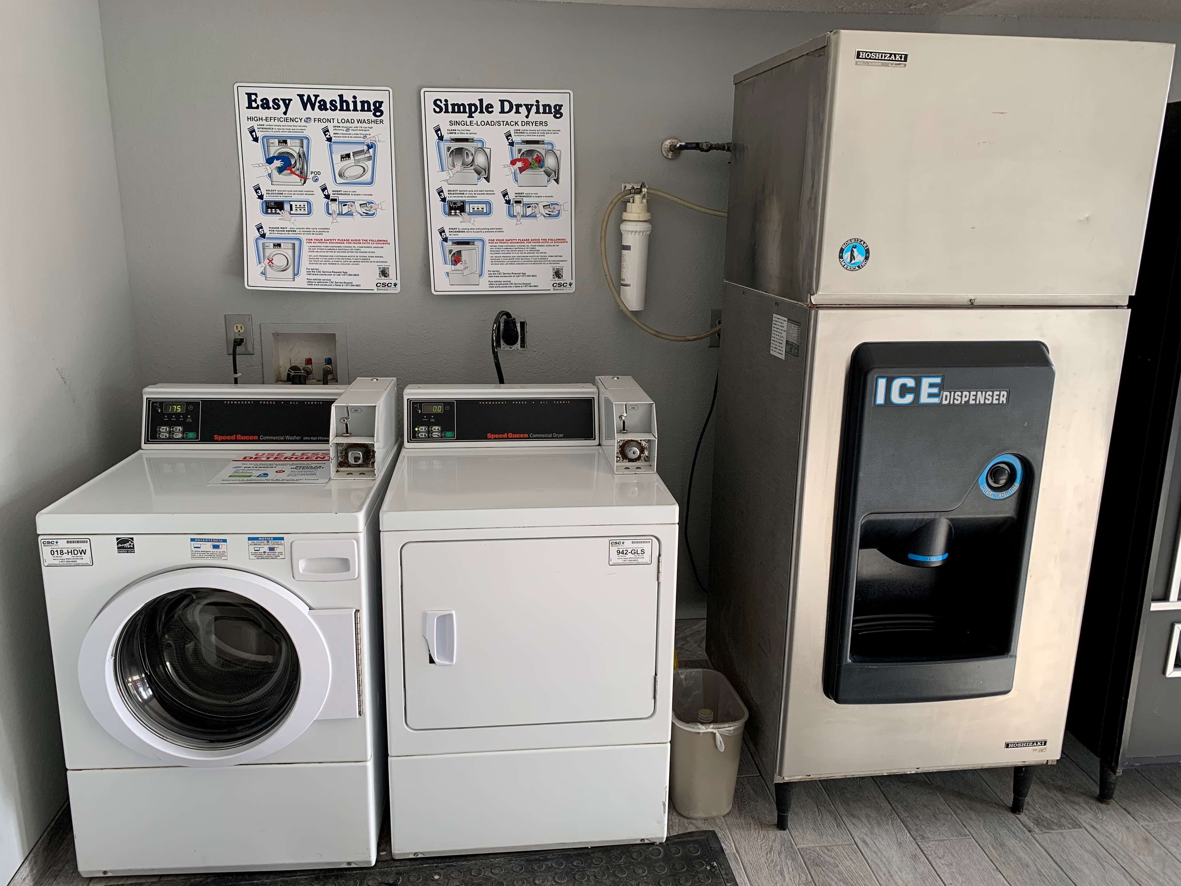 Un espace buanderie équipé de deux machines à laver à chargement frontal, d’un sèche-linge industriel et d’un distributeur de glaçons.