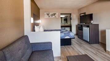 Una habitación de hotel compacta con sofá, cama con colcha estampada, pequeña kitchenette con microondas y televisor, además de un mapa mundial en la pared.