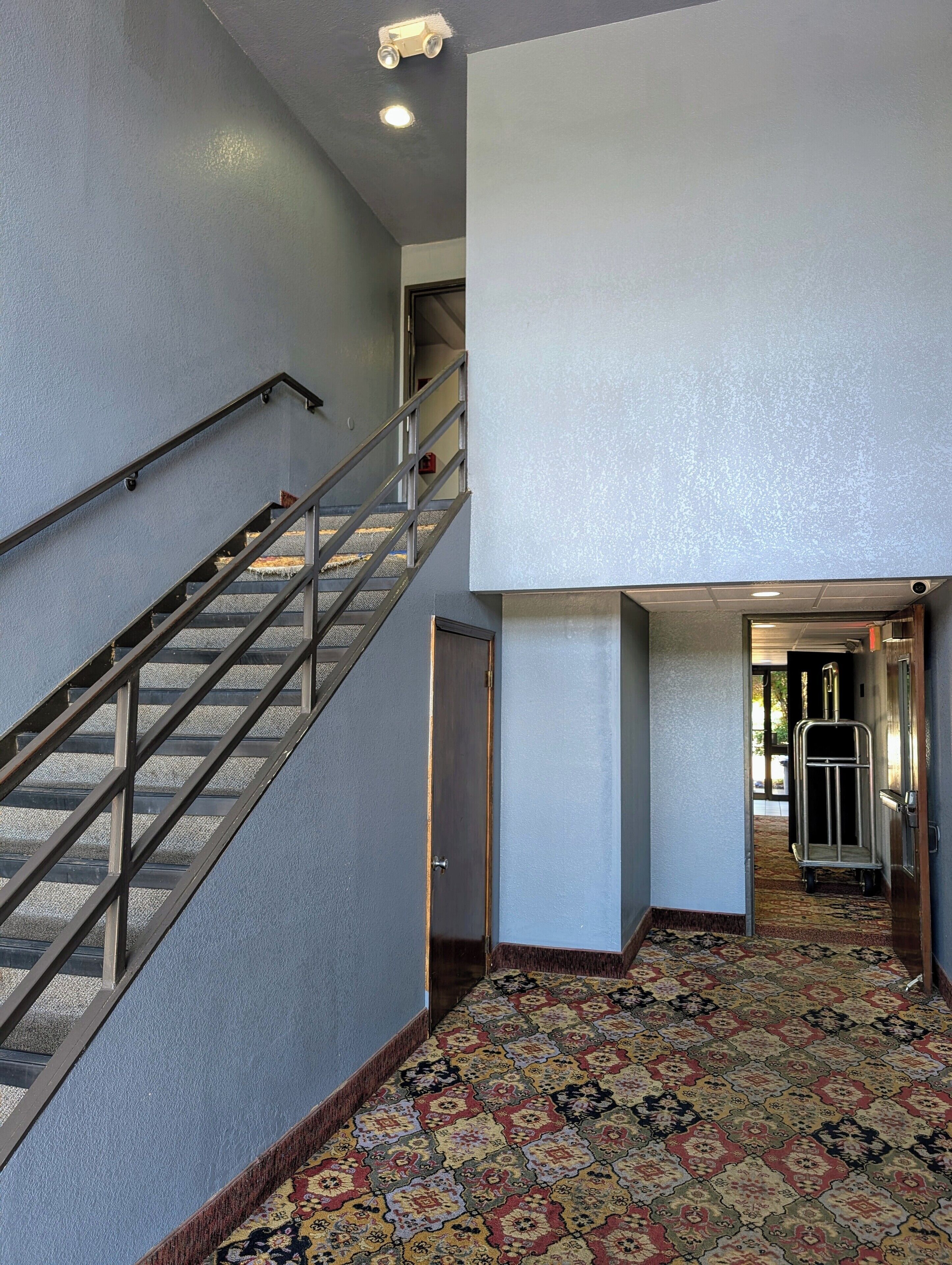 A hotel interior with a staircase, carpeted floor, and a door leading to another room.
