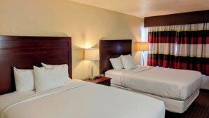 Habitación de hotel con dos camas, cabeceros de madera, lámparas de noche y cortinas a rayas.