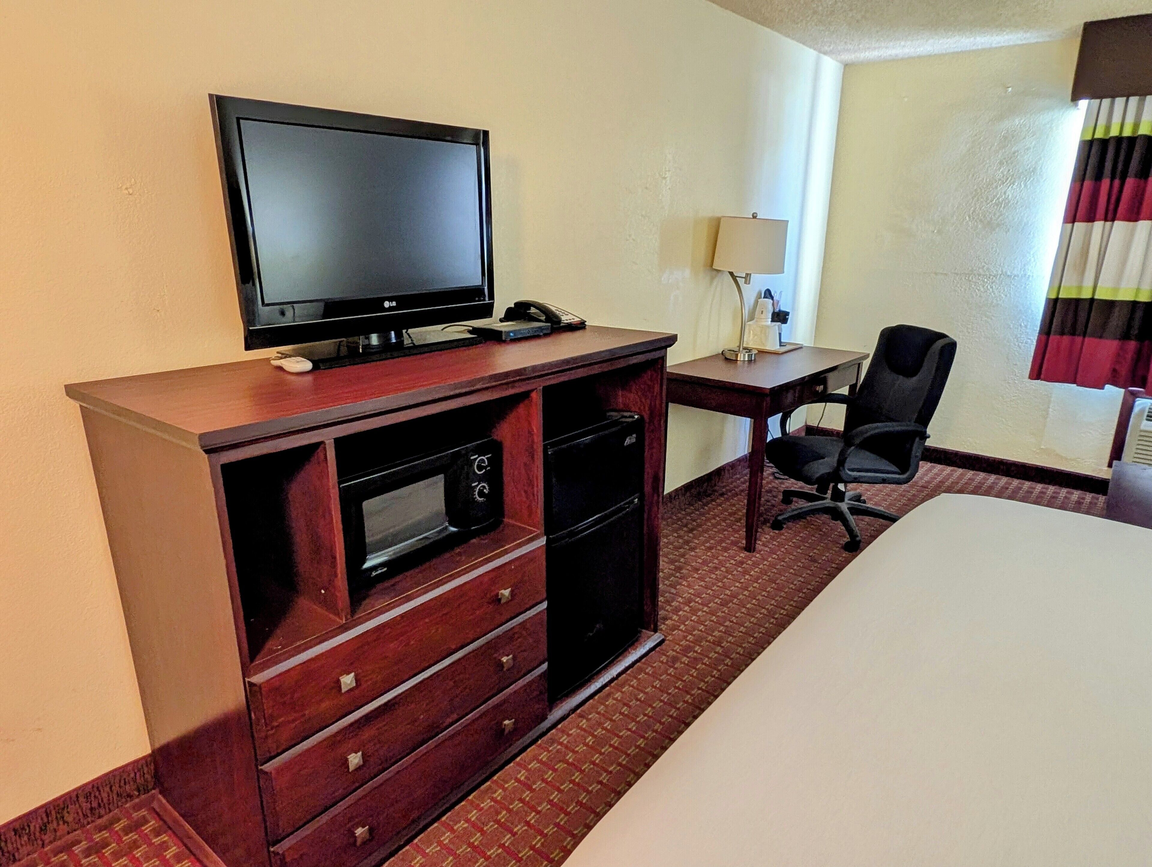 Een hotelkamer met een bed, een bureau met stoel, een televisie, een lamp en een minibar.