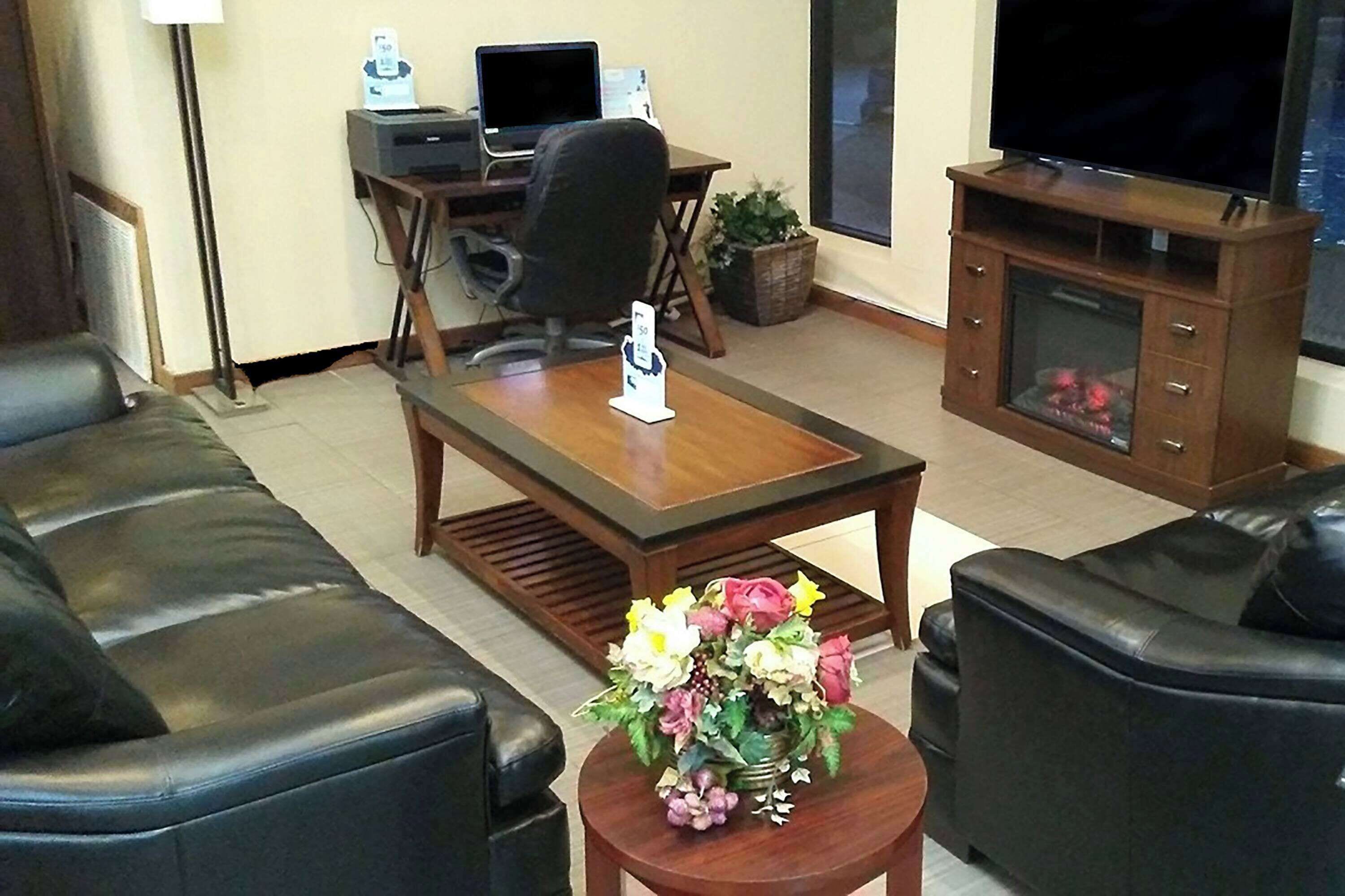 A living room with a sofa, a coffee table with a floral arrangement, a TV on a stand, a desk with a computer, and a fireplace.