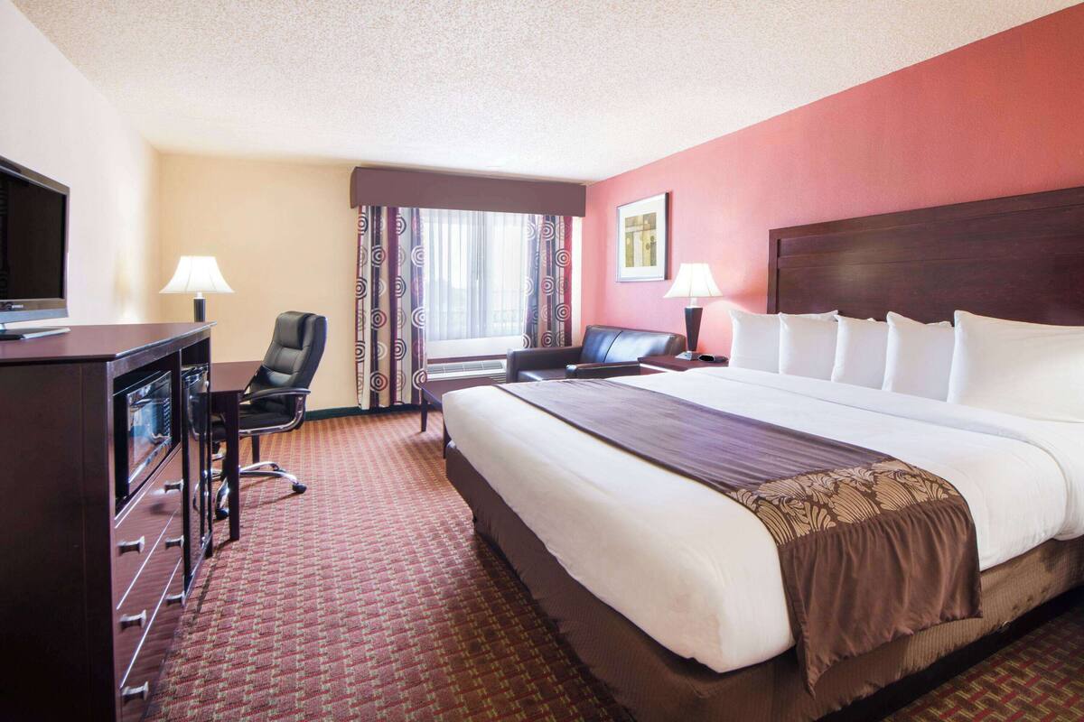 A hotel room with a large bed, a desk with a computer, a chair, and a TV.