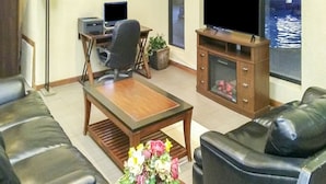 Una sala de estar con sofás de cuero, una mesa de centro de madera, un escritorio con computadora y un televisor sobre un mueble de madera.