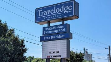 Une enseigne indiquant la présence d’un hôtel Travelodge by Wyndham, mettant en avant ses équipements, notamment une piscine intérieure chauffée et un petit-déjeuner gratuit.