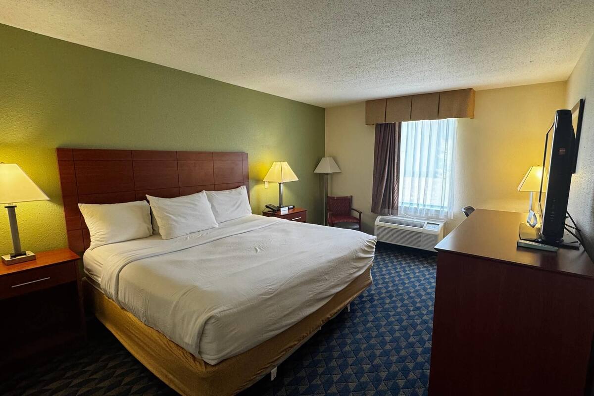 A hotel room with a large bed, two bedside tables with lamps, a desk, and a chair.