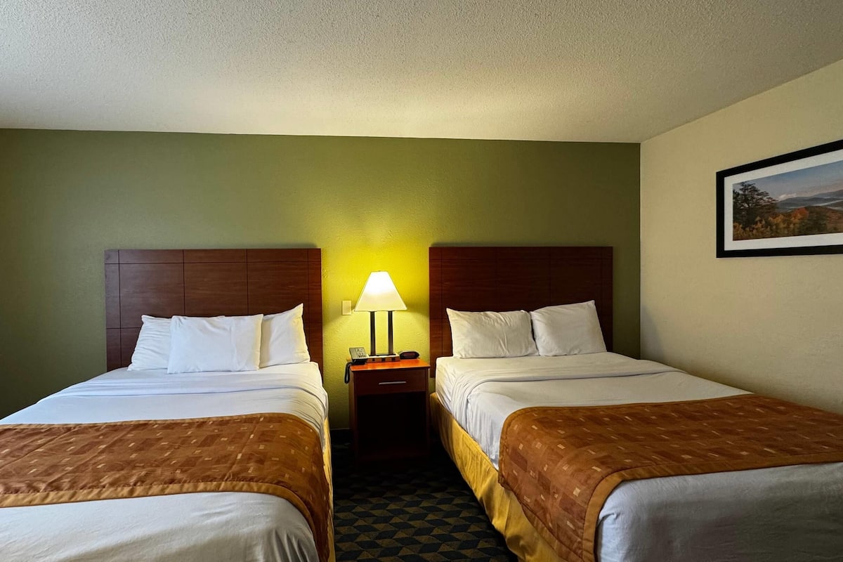 A hotel room with two beds, a nightstand with a lamp, and a painting on the wall.