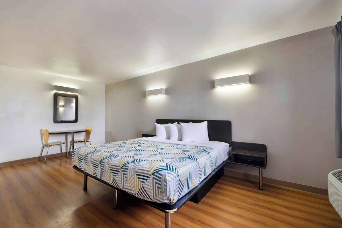 A modern hotel room with a bed, bedside table, chair, and a desk with a chair.