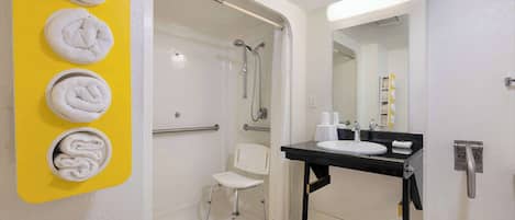 A bathroom with a yellow towel rack, a white chair, a sink with a mirror, and a shower area.