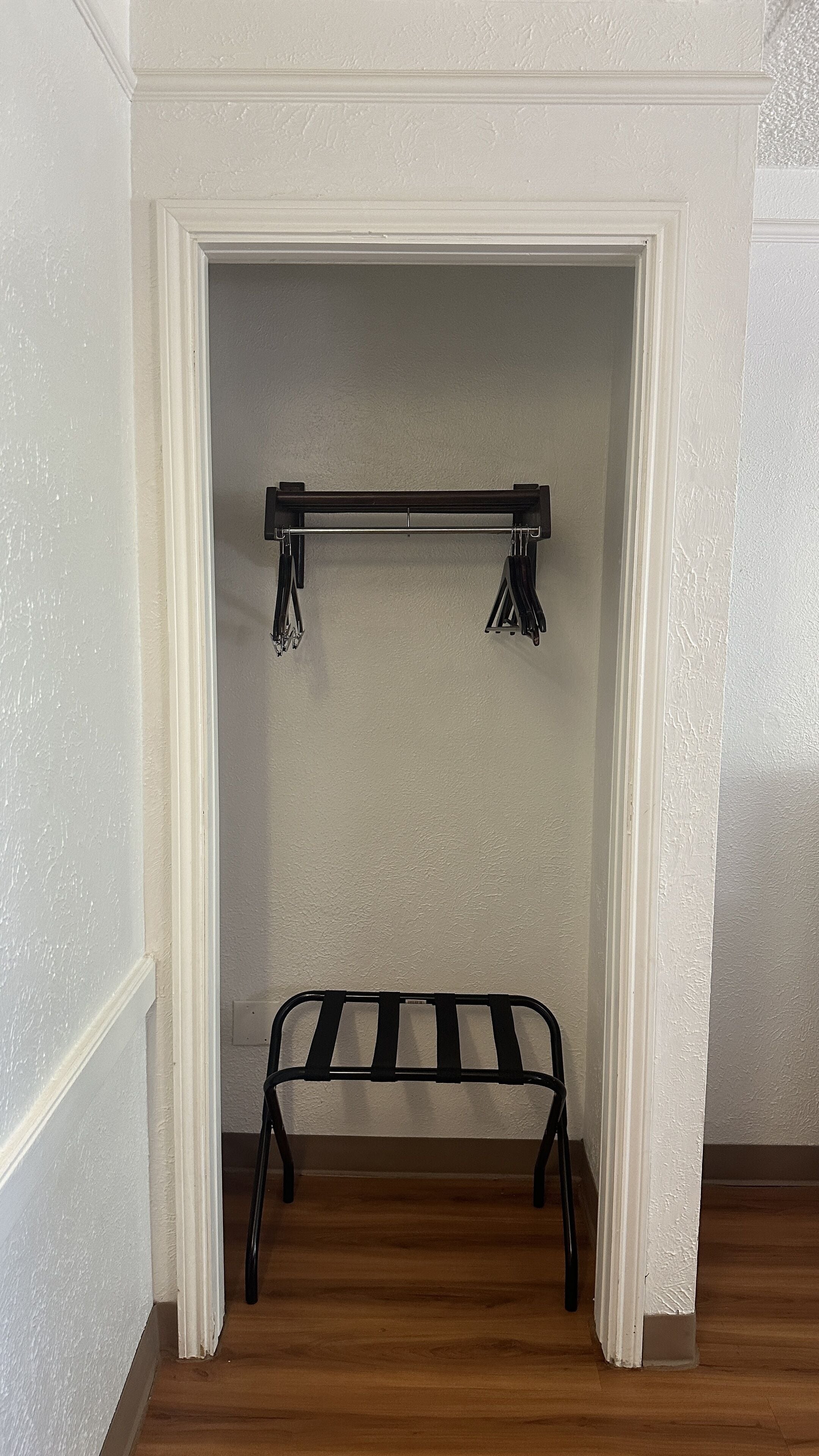 A corner of a room with a white wall, a wooden floor, and a black metal rack with hooks.