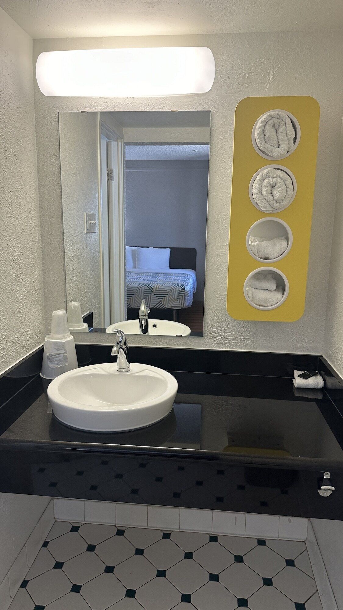 A bathroom with a white sink, black countertop, and a mirror. There is a towel rack with three towels and a bottle of hand soap on the counter.