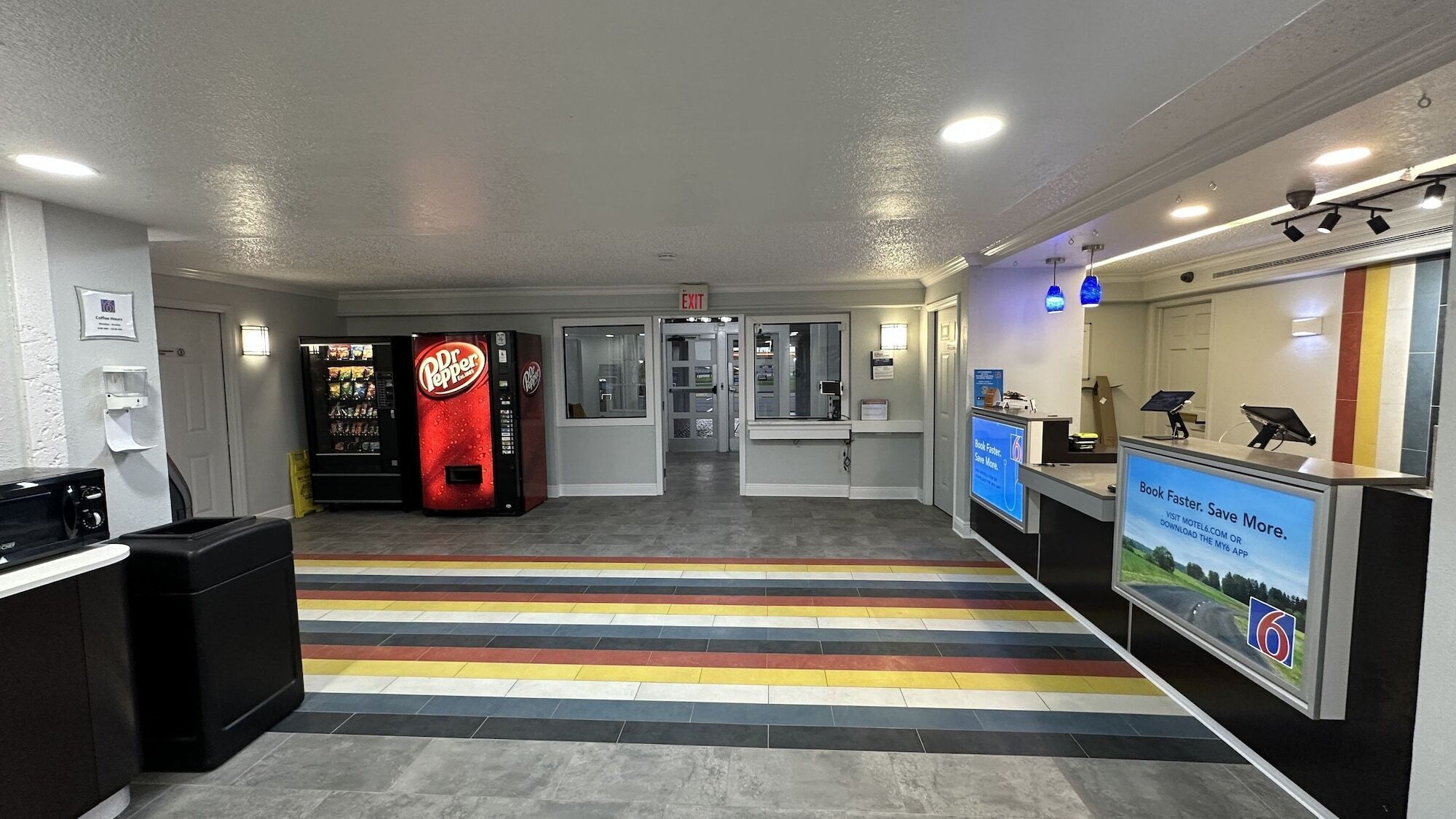 A reception area with a Dr. Pepper vending machine, a counter with a digital screen, and a colorful striped carpet.