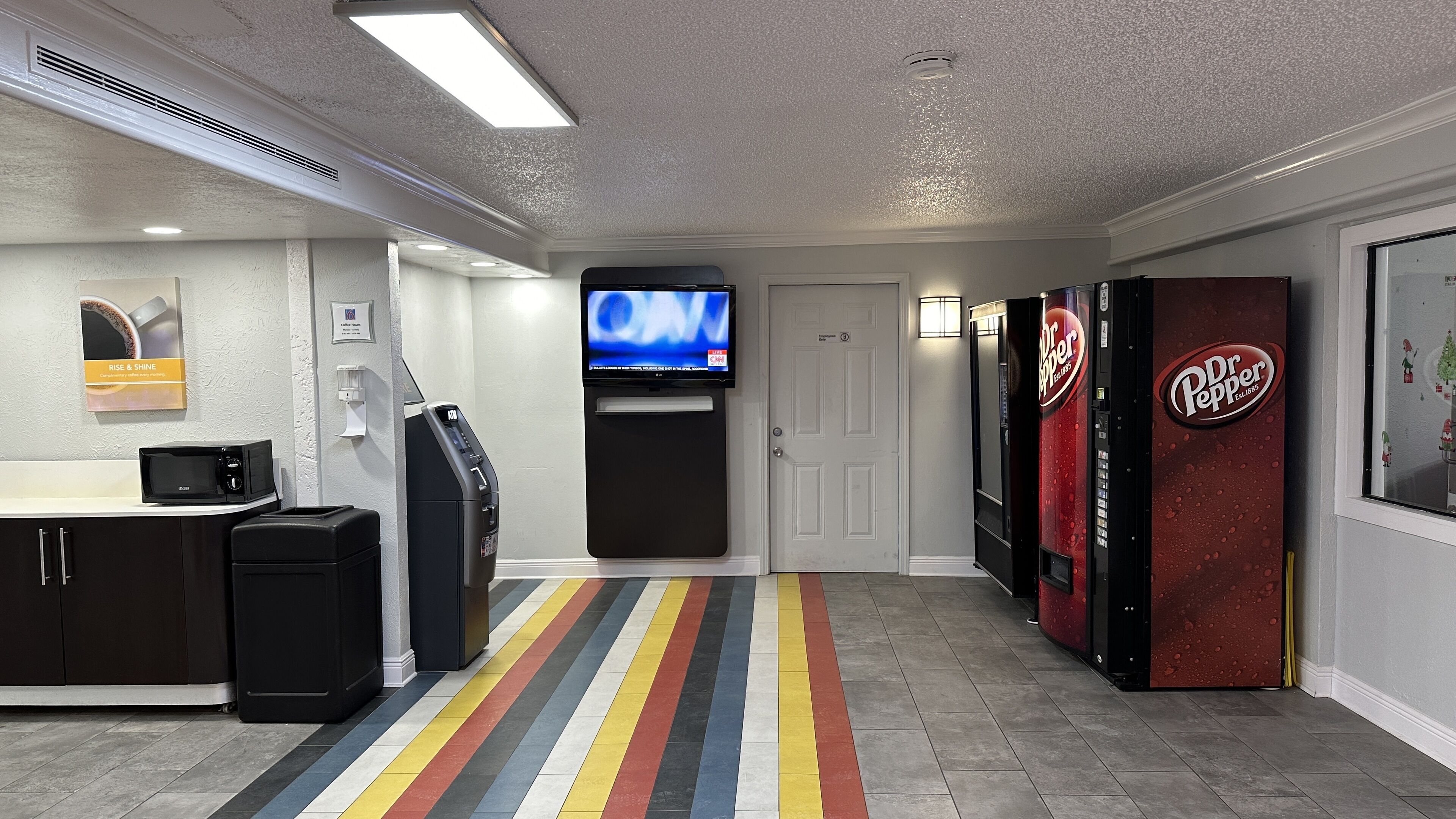 A hotel corridor with a striped floor, a television mounted on the wall, and vending machines.