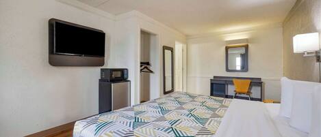 Quarto de hotel com cama, televisão na parede, secretária com cadeira, micro-ondas e espelho.