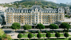 Un hotel grande e histórico con varios pisos, un patio central con árboles y montañas al fondo.