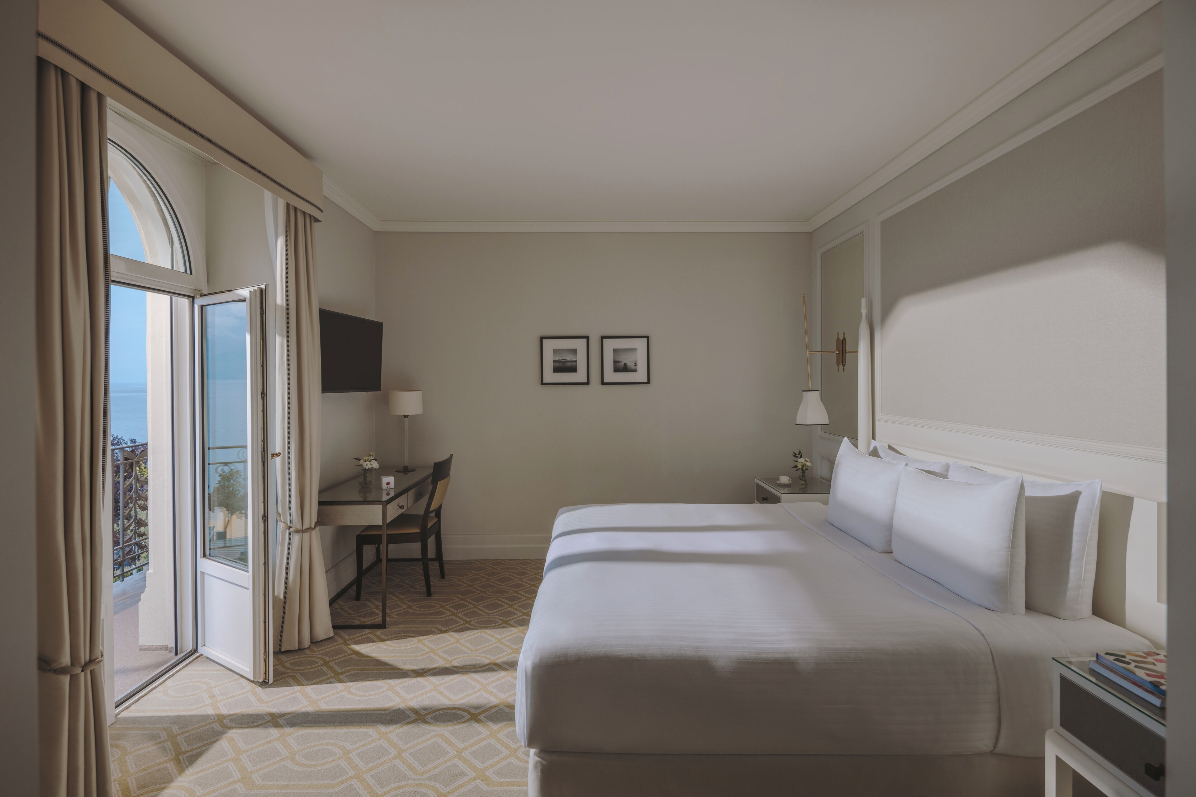 Camera d'albergo con un letto grande, una scrivania, una sedia, una TV e un balcone con tende.