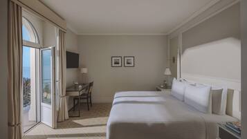 Camera d'albergo con un letto grande, una scrivania, una sedia, una TV e un balcone con tende.