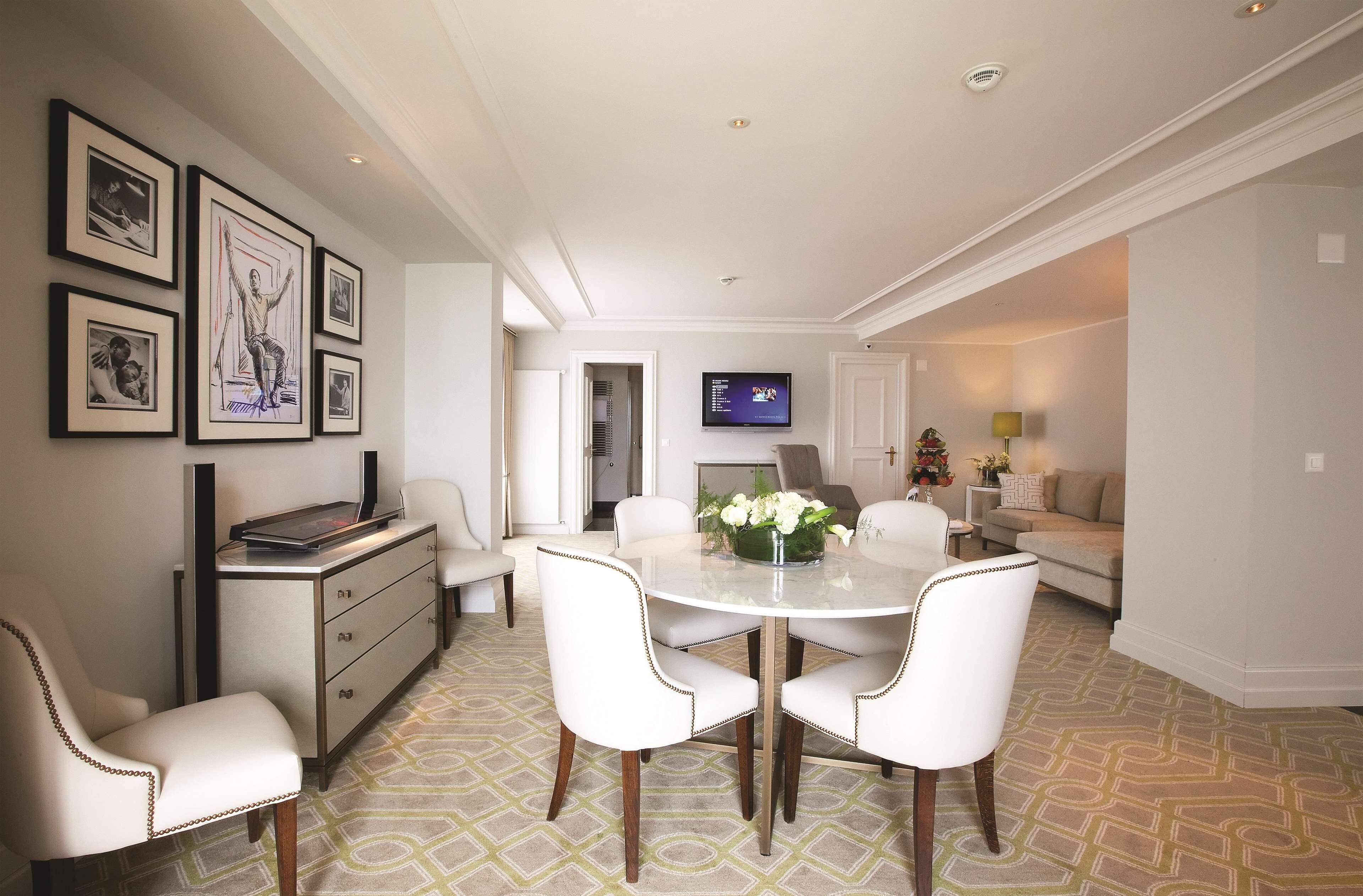 A dining area with a round table, white chairs, and a TV mounted on the wall.