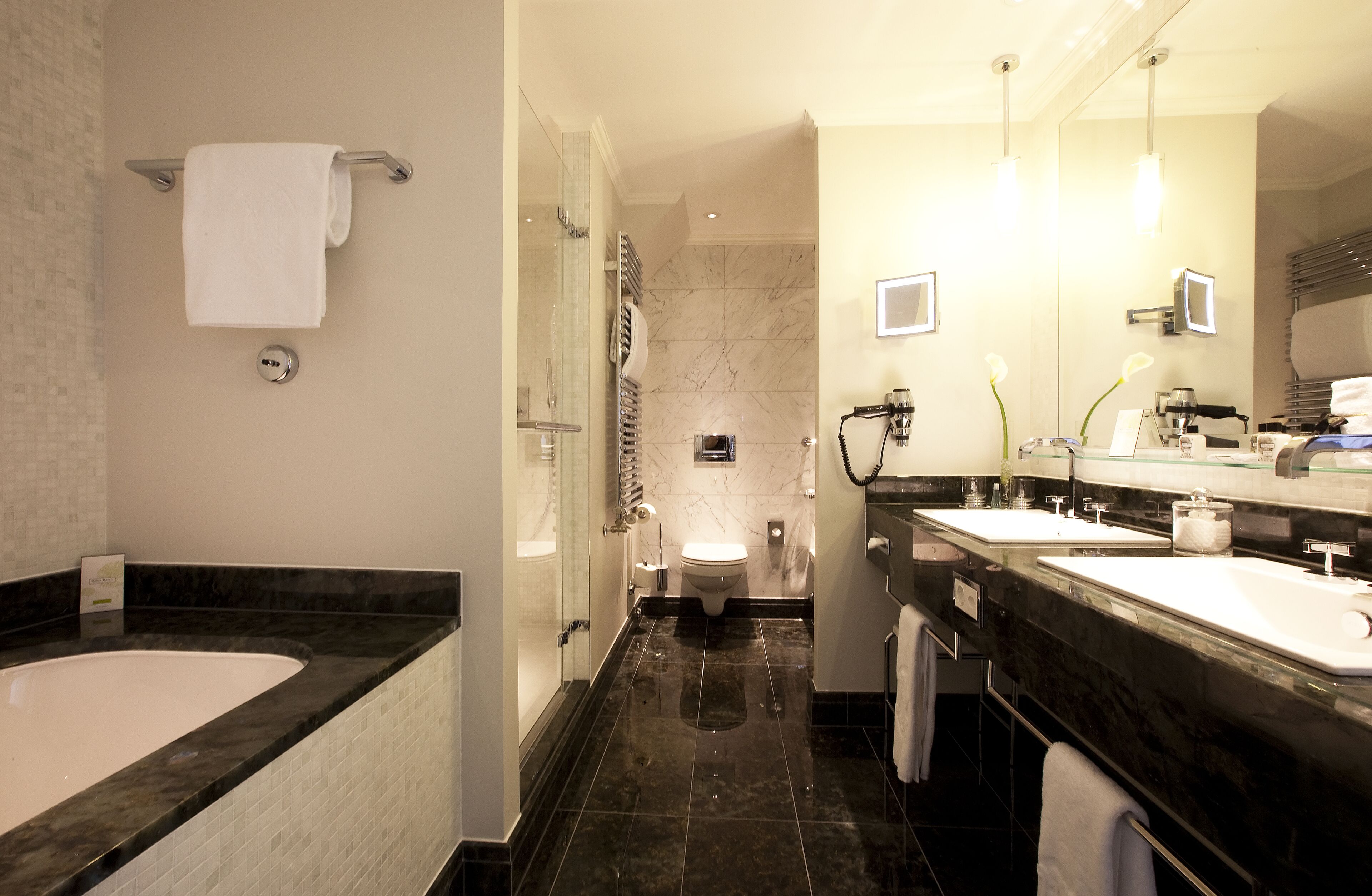 A modern bathroom with a large bathtub, two sinks, a toilet, and a glass shower enclosure.