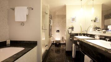 A modern bathroom with a large bathtub, two sinks, a toilet, and a glass shower enclosure.