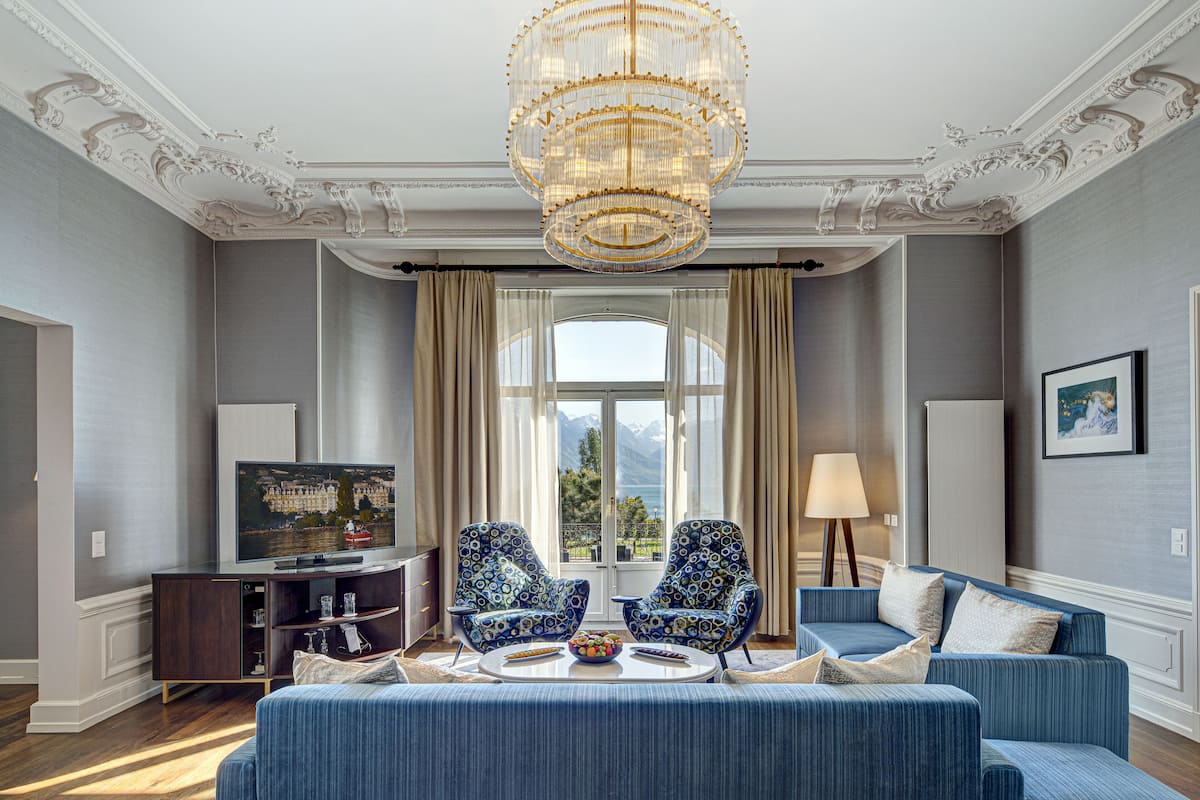 A spacious living room with a large chandelier, a sofa set, a television, and a view of mountains through the window.