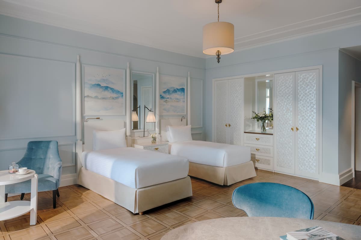 Habitación de hotel con dos camas, una zona de estar con una silla, una mesita y un espejo grande.