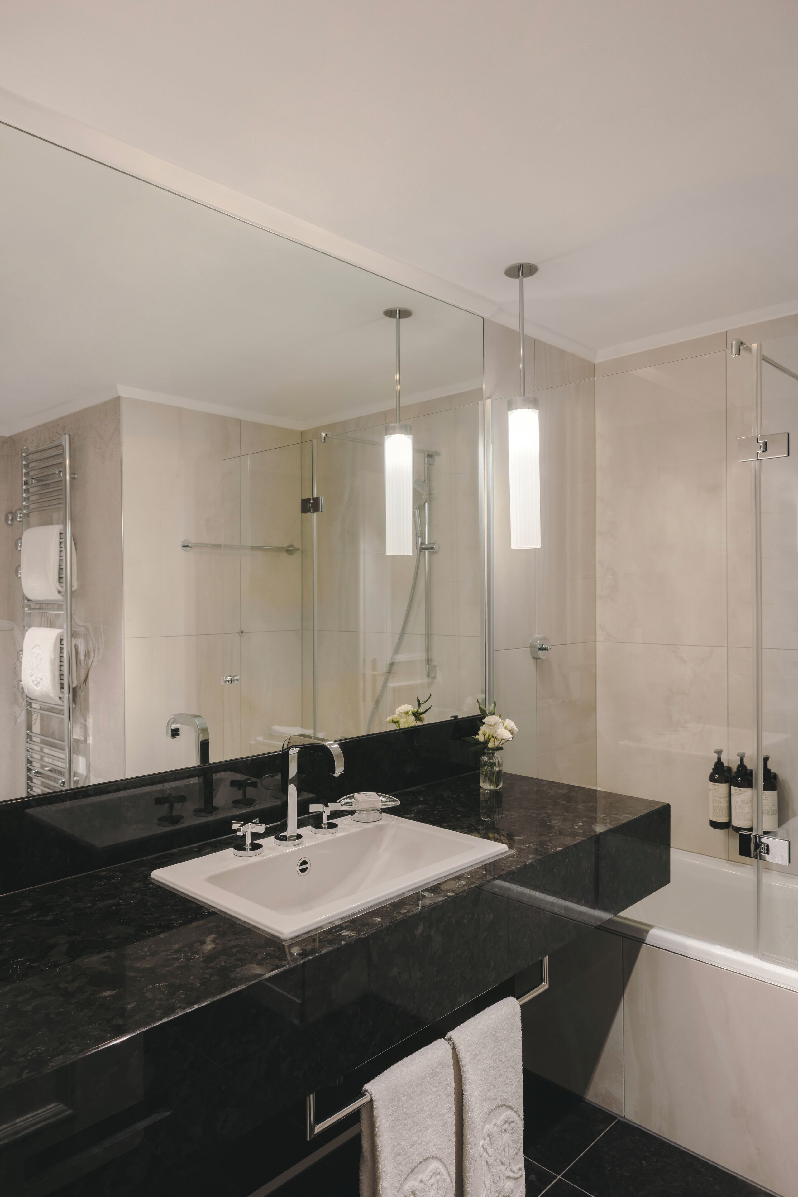 A modern bathroom with a large mirror, black marble countertop, white sink, and a glass-enclosed shower.