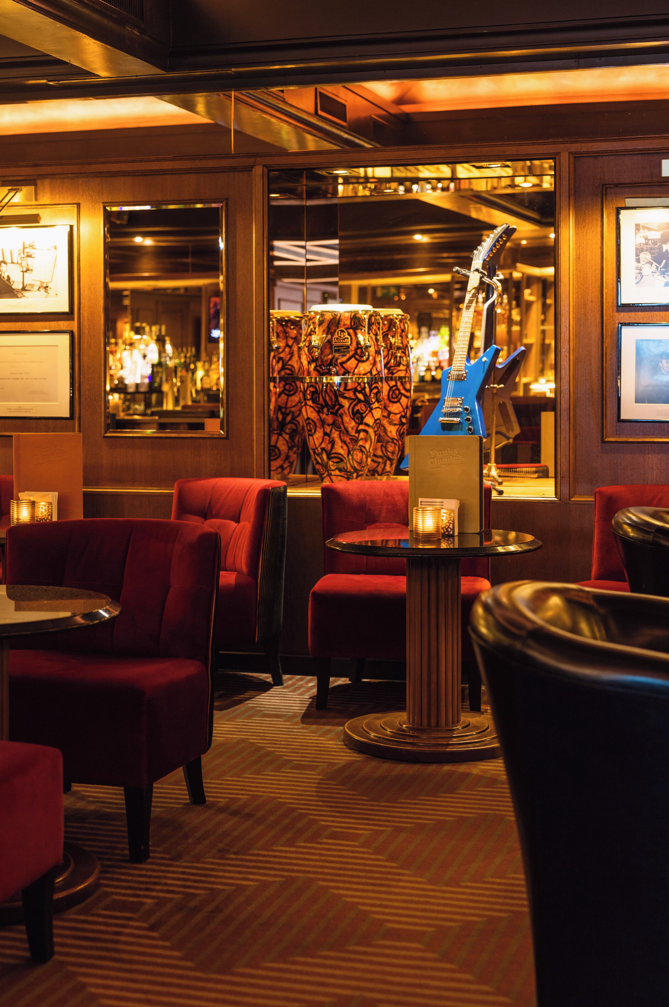 A bar area with red upholstered chairs, a blue guitar, and framed pictures on the walls.