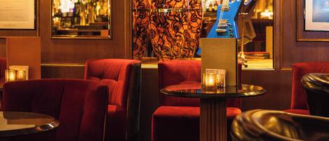 A bar area with red upholstered chairs, a blue guitar, and framed pictures on the walls.