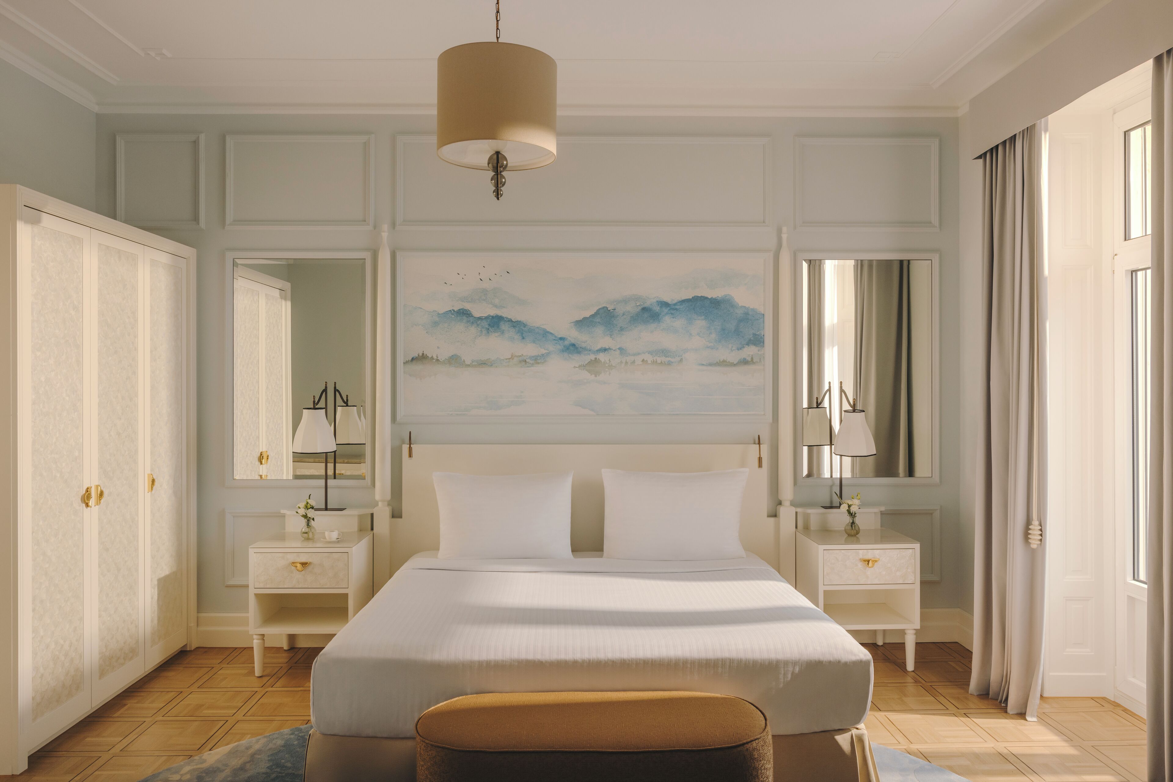 Habitación de hotel con una cama grande, dos mesitas de noche, un aparador, un cuadro en la pared y una ventana con cortinas.