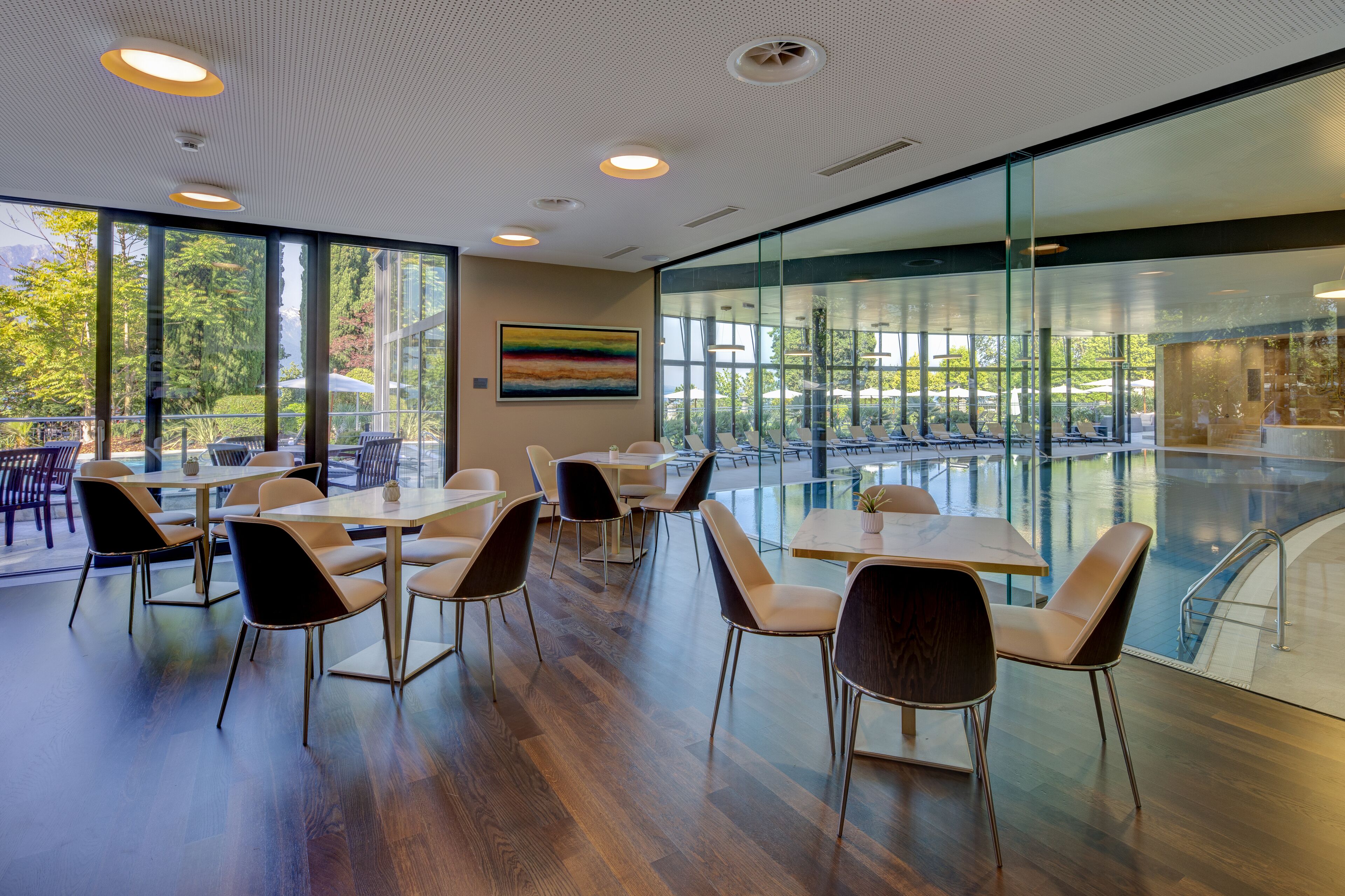 A modern indoor dining area with tables and chairs, large windows, and a view of an outdoor pool.