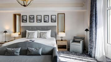 Una habitación de hotel moderna con una cama grande, un sofá gris, una mesita pequeña y una lámpara de pie.